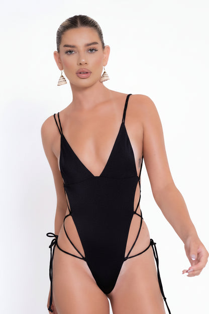 Woman wearing a black swimsuit with thin straps on a white background
